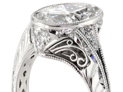 Four sets of three curls make up this filigree engagement ring which also features interior lattice wire work. Ring is shown with an oval brilliant center diamond, hand engraving, and milgrain.