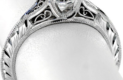 This hand engraved engagement ring is shown with a wheat pattern on both side of a knife-edge shank. Ring is made in white gold and also features filigree.