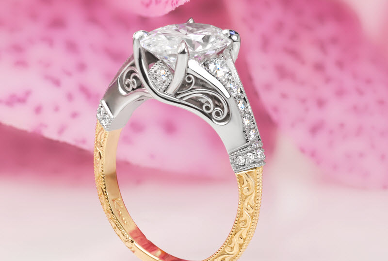 Albany custom two tone engagement ring with an oval diamond held center by four prongs and a band featuring bead set diamonds, milgrain edging, filigree and relief engraving.