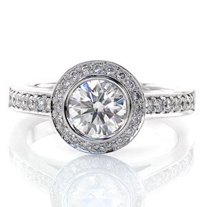 Graceful curves define the elegant Enchantment. The 0.75 carat round brilliant cut center stone is bezel set and surrounded by a micro pavé halo. Curving up to join the halo, the shared prong diamond band is detailed with two bezel set surprise diamonds.