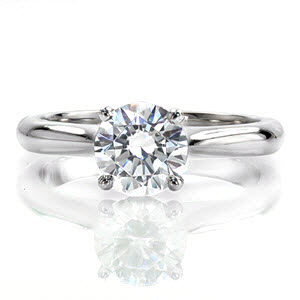 Silk is a classic solitaire with a touch of flair. The contour of the band raises to a cathedral and is accented with pinched shoulders. A captivating 1.0 carat round brilliant diamond is held in a four prong basket slightly above the mounting. The sleek polished finish highlights the luster of the diamond. 