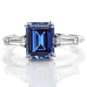 Design 1158 features tapered diamond baguettes flanking each side of the  2.50 carat emerald cut blue sapphire.  Crafted  in platinum, the four double prongs accent the imperial blue of the gemstone. As a continuation of an elegant presence, a tapered band rounds at the bottom of the shank for utmost comfort.