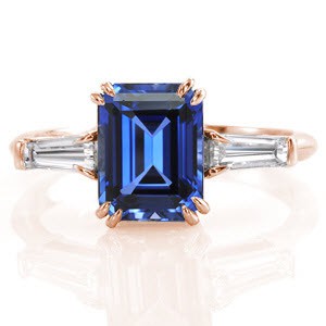 Design 1158 features tapered diamond baguettes flanking each side of the  2.50 carat emerald cut blue sapphire.  Crafted  in platinum, the four double prongs accent the imperial blue of the gemstone. As a continuation of an elegant presence, a tapered band rounds at the bottom of the shank for utmost comfort.