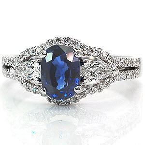 A unique, luscious design, the focus of this piece is all in the rich color of the center stone. On either side is a dazzling pear cut diamond which elegantly compliment the oval cut of the center sapphire. The band splits into two rows of micro pavé hugging the curves of the three center stones.