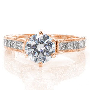 Our Roma design displays regal elegance. A six prong crown gracefully holds a 1.0 carat round diamond. Delicate swooping shoulders with micro pavé diamonds frame the center stone. Channel set princess cut diamonds, hand engraving and milgrain add detail to the band creating an eye catching piece.