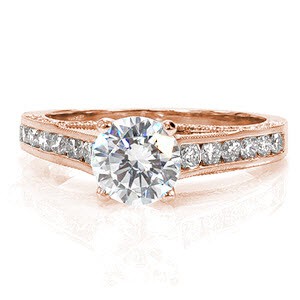 A magnificent design featuring a line of elegantly contoured micro pavé diamonds on each side of the band. The top of the band is detailed with a row of larger, channel set diamonds. The center stone shown is a 1.00 carat round brilliant cut diamond. Milgrain has been added to the edges for texture.