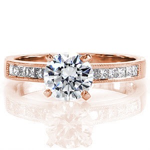 Simply stated, the Princess Petite design is crafted in 18k white gold. The band of gold frames channel set princess cut diamonds and outlined with hand applied milgrain. The 1.00 carat round brilliant cut center diamond is accented by four high polished prongs.