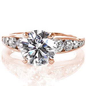 The allure of channel set diamonds, which graduate in size, draw attention to a stunning 2.00 carat round brilliant cut center diamond. Crafted in 14k white gold, the flared band meets the four prong set center stone with a round contour and slightly raised shoulders. 