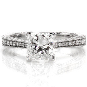 The reverse taper of the band immediately draws attention to the 1.00 carat princess cut center diamond. The stone is secured with chevron prongs which protect its corners. The top of the band is lusciously accented with round diamonds that graduate in size to match the width of the band.