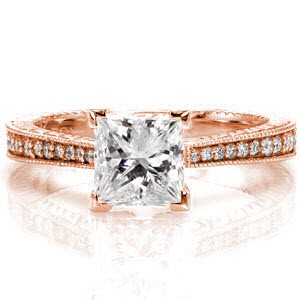 The reverse taper of the band immediately draws attention to the 1.00 carat princess cut center diamond. The stone is secured with chevron prongs which protect its corners. The top of the band is lusciously accented with round diamonds that graduate in size to match the width of the band.