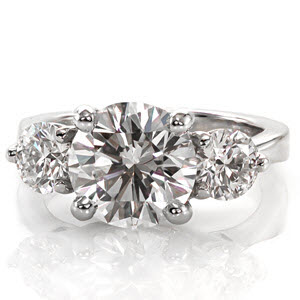 This stunning design is features a 2.20 carat round brilliant cut diamond. The center stone, and two side stones are set in interwoven, trellis patterned prong settings. The graceful curves of the setting, and the reverse tapered band create an elegant ring.