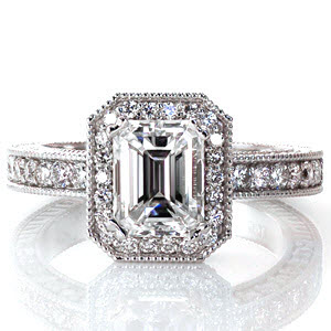 The long linear lines of the emerald cut center diamond are contrasted by the halo of brilliant  micro pavé stones. Matching round diamonds accent under the center setting and on three faces of the band. Engraving and milgrain add an elegant charm, giving this design an antique feel.