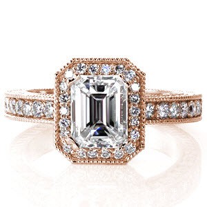 The long linear lines of the emerald cut center diamond are contrasted by the halo of brilliant  micro pavé stones. Matching round diamonds accent under the center setting and on three faces of the band. Engraving and milgrain add an elegant charm, giving this design an antique feel.
