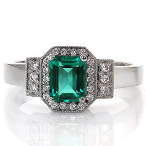 The vivid green emerald is surrounded in a halo of diamonds that mimics the shape of the emerald cut center. The halo and parallel rows of three diamonds are outlined in milgrain detail to contrast the smooth lines of the polished band. The 14k white gold finish compliments the bold color of the gemstone.   