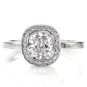This delightful design is fully focused on the cushion shape. It features a 1.00 carat, bezel set, cushion cut center diamond surrounded by a halo of micro pavé which matches the shape of the center stone. The outer edge of the halo is detailed with milgrain to add texture and a refined finish. 