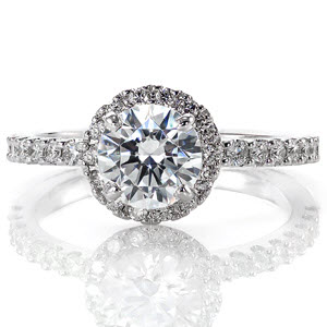 The size of the lovely 0.80 carat round center is enhanced by halo of micro pavé that surround it. Similar stones along the band compliment the multi-faceted center stone and halo diamonds. The slightly raised shoulders allow for matching bands to sit flush on either side of the engagement ring.