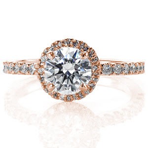 The size of the lovely 0.80 carat round center is enhanced by halo of micro pavé that surround it. Similar stones along the band compliment the multi-faceted center stone and halo diamonds. The slightly raised shoulders allow for matching bands to sit flush on either side of the engagement ring.