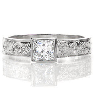 This solitaire design features a wide, flat band crowned with a 0.75 carat princess cut center diamond. The band is embellished with stunning, intricate hand engraved designs and the edges are refined with milgrain texture. The pattern on the band adds an artistic appeal to the overall piece.