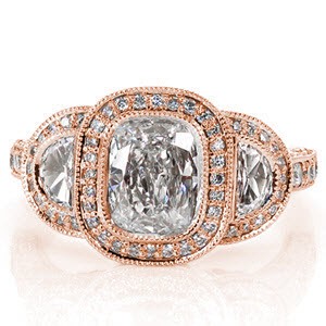 This tantalizing design puts all the focus on the 1.00 carat cushion cut center diamond. On either side of center is a half-moon diamond in a micro pavé halo. The band is lavishly adorned with diamonds on the top and sides. The halo displays pockets of filigree and a butterfly shape for a picturesque side view.