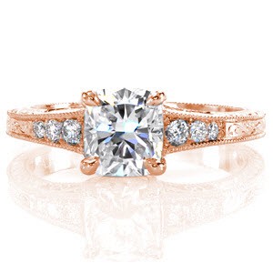 The beautiful shape of the 1.00 carat cushion cut center diamond is splendidly accented by the tapered band of the ring. The bead set side stones taper down in size as well and hand engraving finishes the detailing on top and sides of the band. Filigree curls on the sides add a final delicate touch.