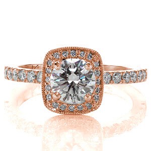 The 1.00 carat round brilliant diamond rests in the center of the cushion shaped halo.  Micro pavé stones outline the top and side of the halo for an endless cushion of sparkle. Two bezel set surprise diamonds create a glamorous side view. Diamonds along the top of the band add brilliance to the white gold metal.