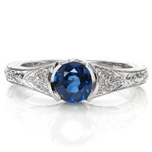 Sapphire Seville is a luxurious antique inspired design displaying a rich blue center gemstone in a half-bezel setting. The vintage inspired elements of hand engraving, milgrain, and filigree give this ring its heirloom-quality detail. The cluster of three diamonds adds brilliance to the white gold mounting. 