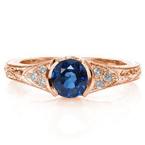 Sapphire Seville is a luxurious antique inspired design displaying a rich blue center gemstone in a half-bezel setting. The vintage inspired elements of hand engraving, milgrain, and filigree give this ring its heirloom-quality detail. The cluster of three diamonds adds brilliance to the white gold mounting. 