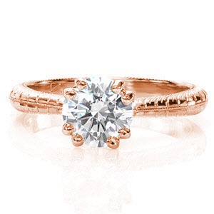 This artistic band uses a reverse taper to put all the focus on the 1.0 carat round brilliant. The milgain knife-edge adds a soft texture and creates separation between the modified wheat hand engraving on each side. Bezel set surprise diamonds at the base of the center stone adds a unique touch to a timeless design. 