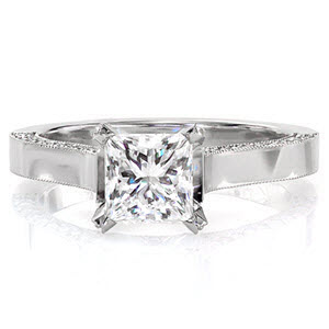 The Princess Arietta is an enthralling design fit for royalty. The sleek lines of the princess cut center diamond are continued down the cathedral setting and into the band which has a flat, high-polished top. The sides of the band dazzle with magnificent flashes of color from the micro pavé.