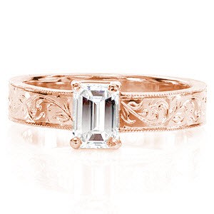 Lorrie features a sophisticated 0.75 carat emerald cut diamond. The long rectangular facets descend towards the center of the stone to accentuate its luster and whiteness. The extravagant pattern of the hand-carved engraving and the textured milgrain edges possess a vintage charm.  