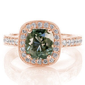 A forest green 1.50 carat sapphire is elegantly displayed in a four prong halo setting. micro pavé diamond accents decorate the design adding radiance and glamor. Filigree curls in the windows, hold diamonds and add a unique element. Hand engraving and milgrain detail complete the ring. 