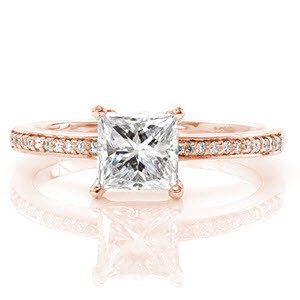 The crisp lines of the Princess Milano design bring out the most desirable qualities in a four prong set 1.00 carat princess cut center diamond. Hand set micro pavé diamonds top the 14k white gold band. Adding a splendid touch, surprise diamonds within the prong basket.