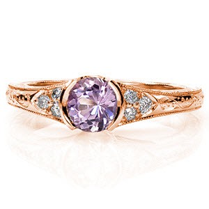 The Sapphire Seville blends intricate details of handcrafted filigree and precise hand engraving. The 0.75 carat round cut natural purple sapphire is dressed with side stones in a triangular arrangement. Completing the antique style, milgrain edges frame the rings outline.