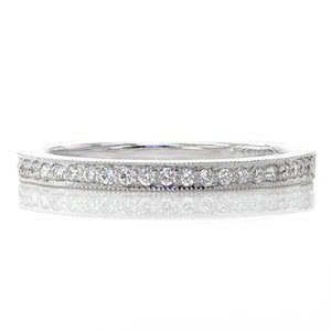 This traditional wedding band features a straight edged band adorned with a row of micro pavé diamonds. The edges of the ring are textured with milgrain beading that is a perfect accent to the prongs of the stones. This design has a low profile and is created to sit flush against the Amante engagement ring.