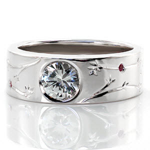 This wide contemporary band was custom designed with hand engraved organic patterns. There are lovely pink sapphires bezel set throughout the engraved design. The center stone is a bezel set 0.80 carat round brilliant cut diamond. The high polish of the ring creates a beautiful contrast with the details.