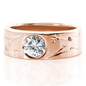 This wide contemporary band was custom designed with hand engraved organic patterns. There are lovely pink sapphires bezel set throughout the engraved design. The center stone is a bezel set 0.80 carat round brilliant cut diamond. The high polish of the ring creates a beautiful contrast with the details.
