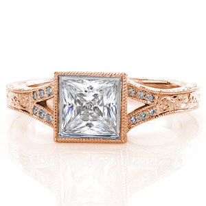 Our Vienna design has many intriguing details. The 1.00 carat princess cut center diamond is bezel set in a split shank band with micro pavé detail. Below, hand engraving elegantly accents the rest of the band. From the side, you can see filigree and surprise diamonds.