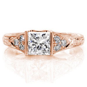 The Princess Seville displays a 1.0 carat square center stone in a half-bezel setting. The band tappers from a lovely three stone array of diamonds to intricate scroll hand engraving. The side profile of the ring displays hand-formed platinum filigree and a hand engraved wheat pattern.