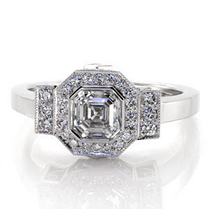 Art Deco inspiration is reflected in Design 2163. The center displays a full bezel set, .90 carat, asscher center with a octagonal micro pavé diamond halo. The design merges into a rectangular row of bead set diamonds and polished band. Two carrÃ© cut diamonds and filigree curls decorate the sides.  