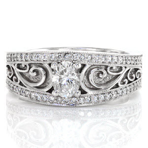 This dazzling ring uses lovely filigree curls to highlight the 0.50 carat oval cut center diamond. The center stone and filigree is encompassed by two rows of micro pavé with milgrain texture on the edges. These details blend seamlessly together to create a unique, antique inspired wide band.