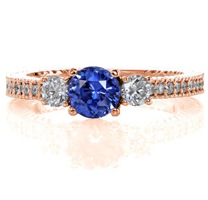 Modern charm meets a timeless three stone classic in this contemporary engagement ring. The deep blue 0.80 carat round sapphire is intensified between the two round brilliant diamonds. Micro pavé stones heighten the beauty of the textured band for a unified look. 