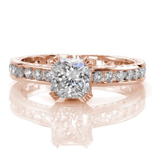 A gleaming 1.00 carat radiant cut center diamond is captured by micro pavé covered prongs with ribbed detail. The elegant 14k white gold band is hand engraved which frames a row of round cut channel set diamonds. Two round pink sapphires are bezel set under the basket adding a surprising touch of color.