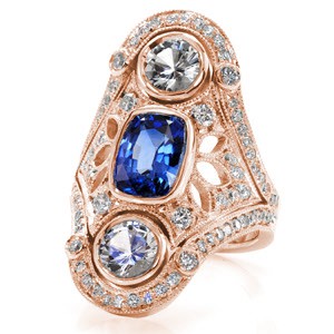 This vintage inspired wide ring design features a 2.00 carat royal blue sapphire. The vertical design also features two large full bezel set diamonds. The ornate pattern is decorated with pierced elements that are embellished in micro pavé set diamonds. This design is truly a statement piece.