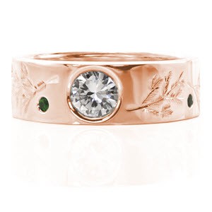 This custom design features unique engraved designs of pine branches. The center stone is a bezel set 0.80 carat round brilliant cut diamond. The wide band also has vivid green emeralds set in between the engraving. The wide band adds a contemporary touch to the ring.