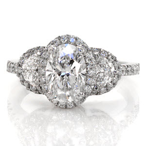 This halo engagement ring features a 1.00 carat oval shape center diamond and two half moon shaped diamonds. The center stone is set with a double prong on each corner. Around these three stones is a halo of micro pavé set diamonds. Both sides of the design feature hand wrought filigree in three pockets. 