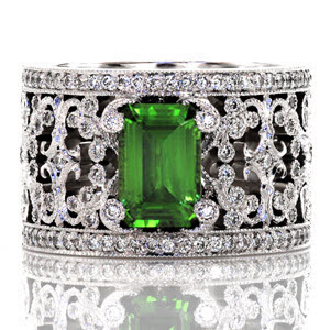 Intricate pierced scrolls created in 14k white gold and adorned with bead set diamonds. The Britty design showcases the emerald cut green gem stone with distinction by four diamond capped prongs. Two rails of shared prong round diamonds are finished with hand applied milgrain on our Knox Signature heirloom band.