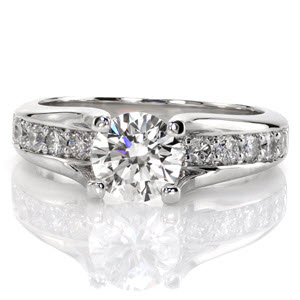This magnificent design features a 1.00 carat round brilliant cut center diamond that is raised above the band. The prongs are formed from the high polished edges of the band which elegantly swoop up to display the center stone. The band is embellished with diamonds that go all the way under the center stone. 