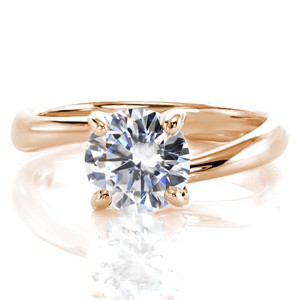 This lovely solitaire design features a unique bypass shank that beautifully frames the center stone. The 1.00 round brilliant cut diamond is elegantly held in a four prong style mounting. The prongs gracefully taper to a wider size for additional support at the base. 
