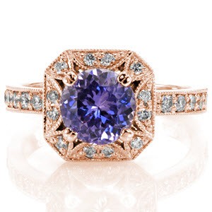 The Lotus Sapphire design is elegantly crafted in 14k white gold and presents a rich, violet round cut natural sapphire. Elements of the ring include detailed prongs, hand applied milgrain and bright-cut bead-set diamonds. The square beveled edge halo is joined by a band of round diamonds.