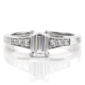 This elegant ring uses the smooth, straight lines of the band to compliment the straight lines of the 0.80 carat emerald cut center diamond. The three round brilliant cut diamonds on either side of the center stone are a beautiful contrast. These side stone graduate in size to match the slight flare of the band.